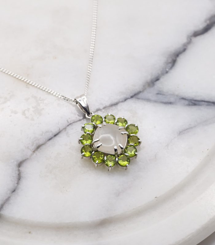 Elegant oval moonstone pendant encircled by 12 vibrant green peridot stones, set in polished 925 sterling silver, showcasing a stunning contrast of lunar glow and verdant sparkle.